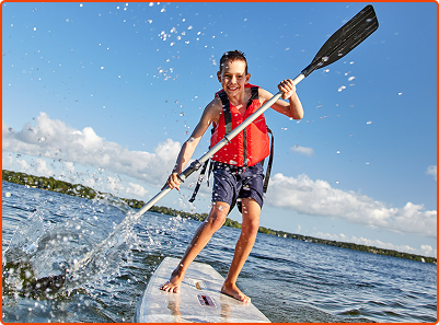 kid standing on paddle board on lake